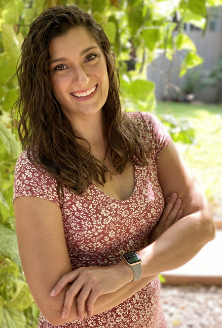 Melissa is wearing an orange and white floral dress. She has shoulder length brown hair.