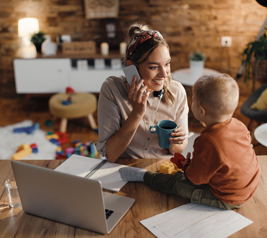 A woman sits with her toddler while on the phone