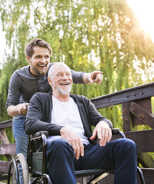 An adult son pushing his elderly father in a wheelchair. They are laughing and having a good time.