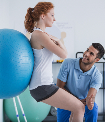 A physical therapist assists a client using a yoga ball