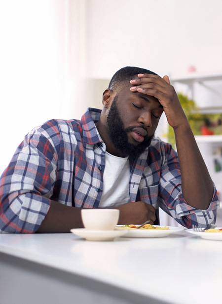 A man sits at the kitchen table holding his head in frustration.