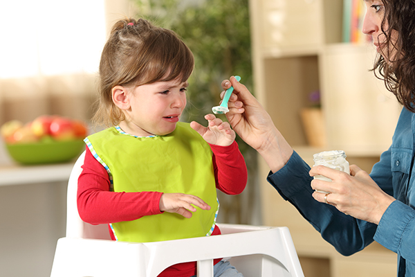 Toddler crying at lunch time sitting in a highchair in the living room at home with a homey background