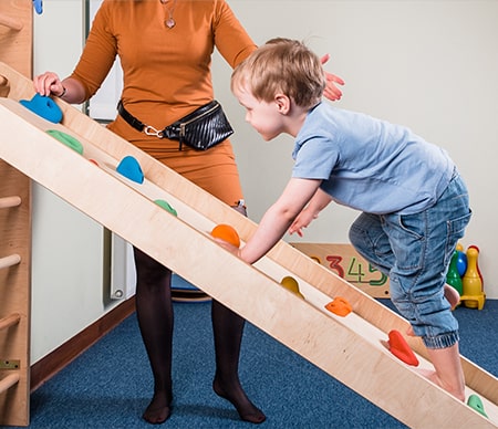 A young boy is climbing a ladder at 45 degrees with his mom spotting him, cheering him on.