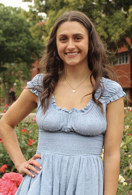 Talia has dark hair and glasses, wearing a cream colored shirt.